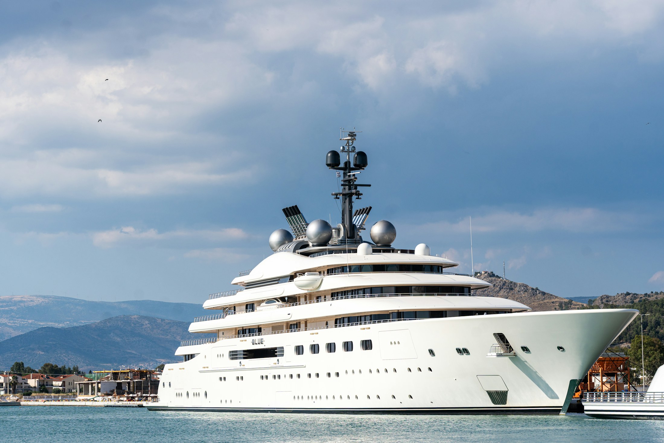 A white superyacht moored against a mountain harbor