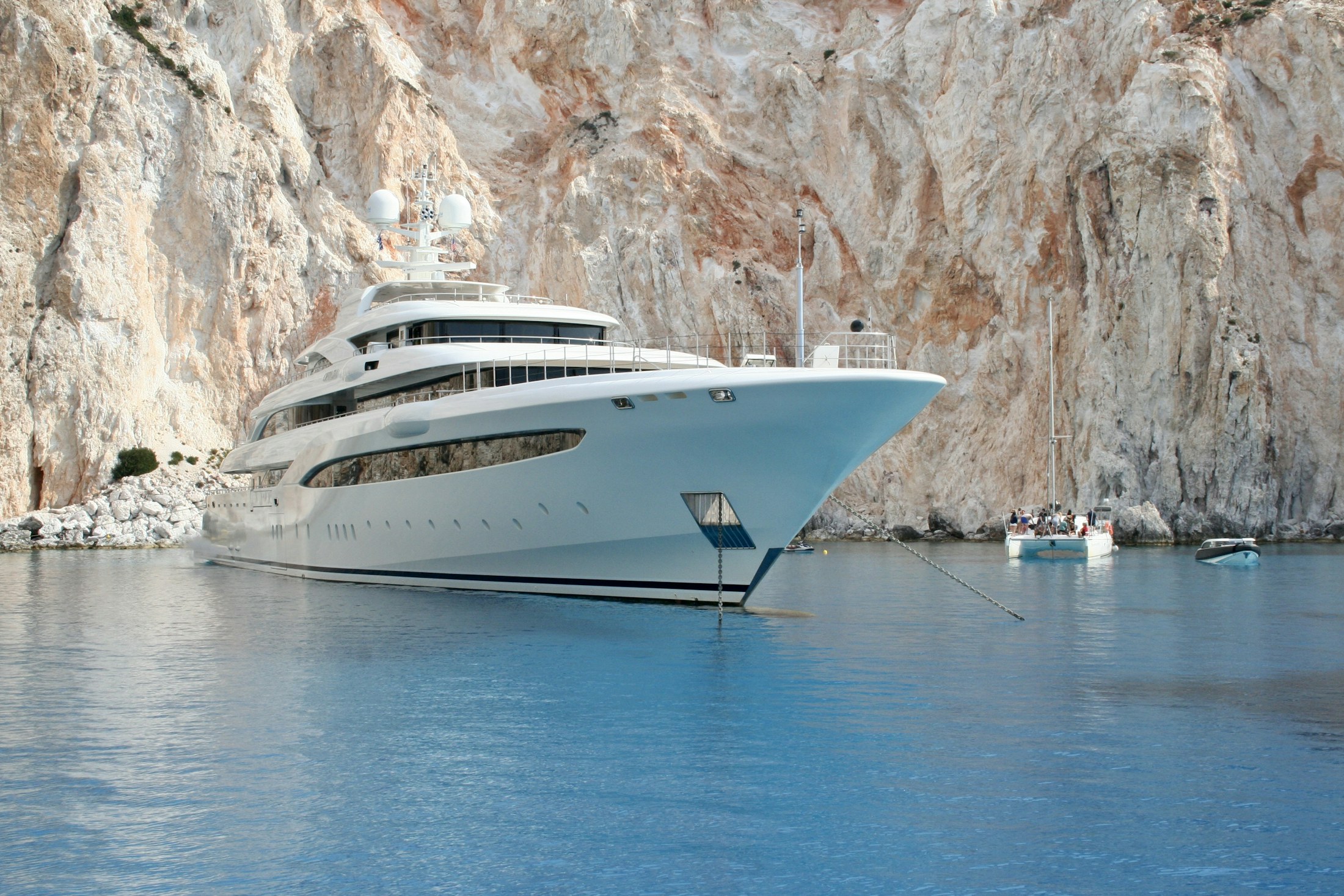 A white motor yacht anchored beside a sunlit cliff